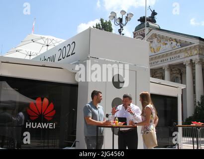 (220707) -- SOFIA, July 7, 2022 (Xinhua) -- People talk during Huawei Enterprise ICT Roadshow 2022 in Sofia, Bulgaria, July 7, 2022. Huawei, a Chinese tech giant in information and communication technology (ICT), showcased its latest solutions during its Enterprise ICT Roadshow 2022 here on Thursday. Huawei's latest products, such as Campus Networks, full-stack Data Centers, and Huawei Clouds that provide stable and reliable cloud services, were presented in a truck in front of the National Theater 'Ivan Vazov' in the heart of Sofia, the capital of Bulgaria. (Photo by Marian Draganov/Xinhua) Stock Photo