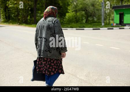 Pensioner in Russia. Grandma is outside in summer. Old woman on road. Poor clothes on person. Stock Photo