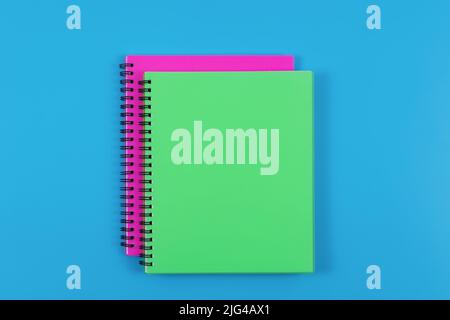 Top view of green and magenta closed spiral journals isolated on blue table background. Blank space. Stock Photo