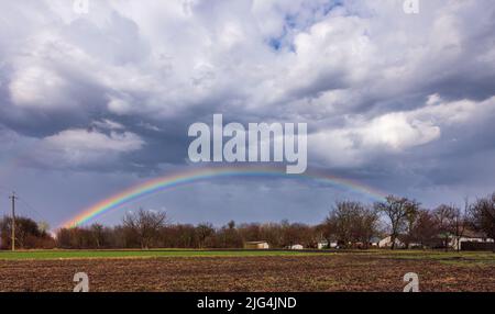 Rainbow in the clouds over village houses Stock Photo