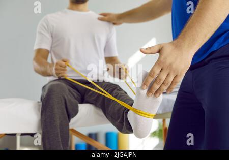 Man doing physical exercises with elastic band at physiotherapy and rehabilitation clinic Stock Photo