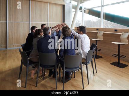 Team of employees joining their hands while sitting in a circle at a corporate meeting Stock Photo