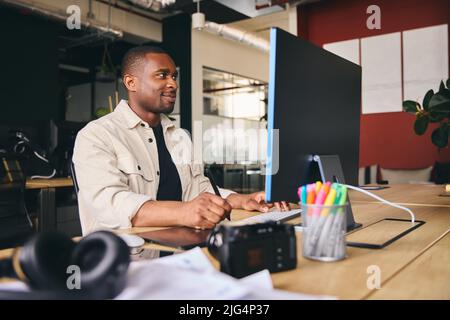 Young Black Male Advertising Marketing Or Design Creative In Modern Office Sitting At Desk Working On Computer Stock Photo