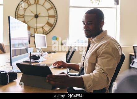 Young creative black man working on computer in modern office at desk on tablet computer smiling Stock Photo