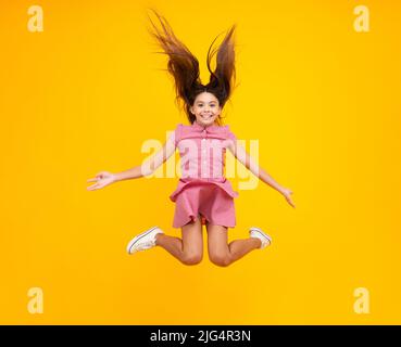 Amazed teen girl. Full size photo of positive teen girl jump with movement summer dress, fashion kids outfit isolated over yellow background. Teenager Stock Photo