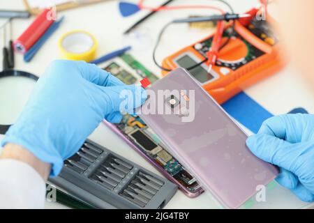 Technician repairs broken smartphone at table in workshop Stock Photo