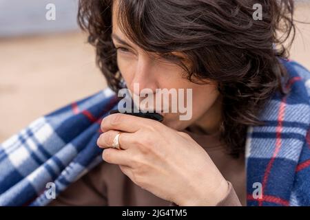 woman drinks hot tea from a thermos while sitting on the beach  Stock Photo