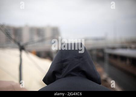 Black hood outside. Unknown person in city. Hidden face. Anonymity in urban environment. Stock Photo