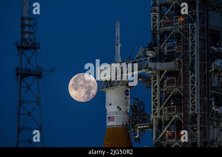 A full moon rises over the NASA Artemis I Space Launch System rocket with the Orion spacecraft aboard a mobile launcher at Launch Complex 39B, at the Kennedy Space Center, June 14, 2022, in Cape Canaveral, Florida. The SLS and Orion are being prepared for a wet dress rehearsal to practice timelines and procedures for launch. Stock Photo