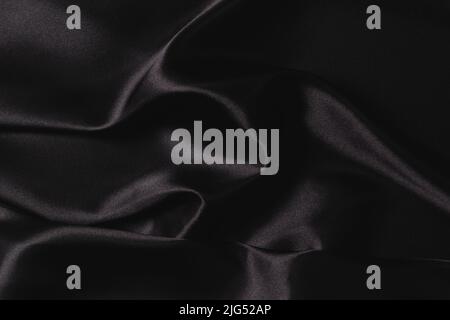 Abstract monochrome elegant luxury cloth background. Black color background with drapery and wavy folds of luxurious silk satin material. Top view Stock Photo