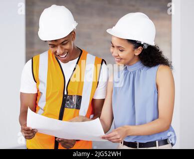 Im pleased with these. Shot of two young contractors standing inside together and looking at building plans. Stock Photo