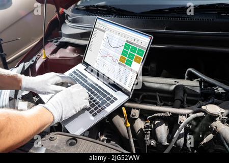 Young Male Mechanic Using Laptop While Examining Car Engine Stock Photo