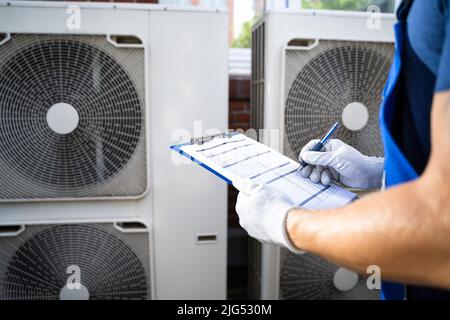 Two Electricians Men Wearing Safety Jackets Checking Air Conditioning Unit On Building Rooftop Stock Photo