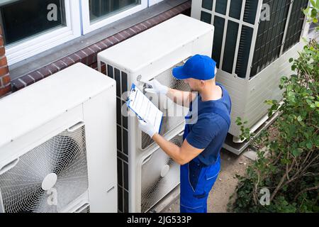 Two Electricians Men Wearing Safety Jackets Checking Air Conditioning Unit On Building Rooftop Stock Photo