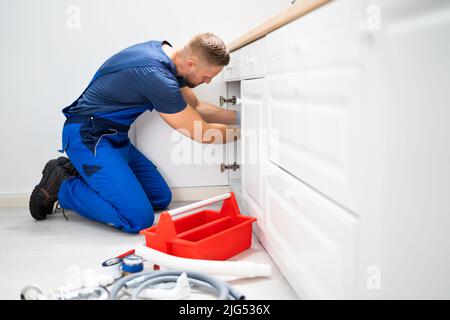 Male Plumber In Overall Fixing Sink Pipe Stock Photo