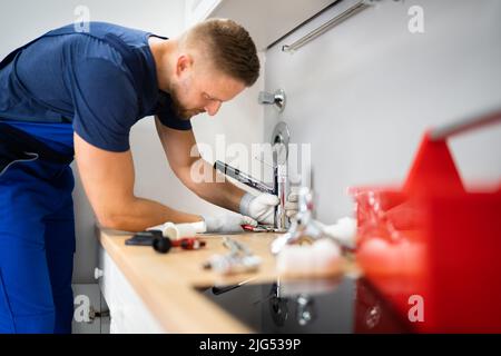 Happy Young Male Plumber Fixing Faucet In Kitchen Stock Photo