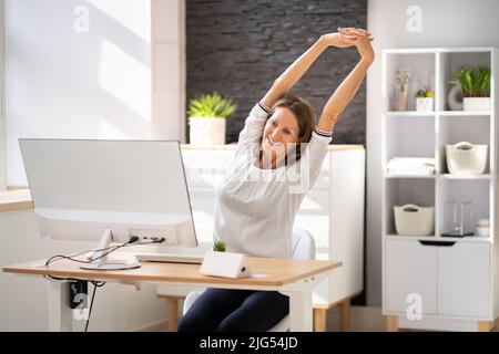 Woman Stretches At Office Desk. Stretch Exercise On Chair Stock Photo