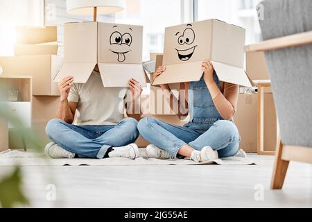 Silly times in abundance. Shot of a couple wearing boxes with smiley faces drawn on them on their heads while moving house. Stock Photo
