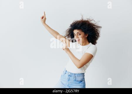 SEASONAL SUMMER SALE OFFER CONCEPT. Enjoyed pretty Latin female with waving afro hair smiling, look at camera, show copy free space. Cool offer for ad Stock Photo