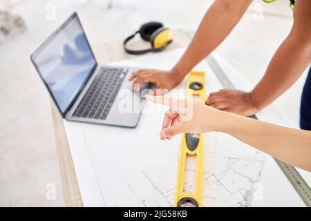 Lets work with that first. Cropped shot of two unrecognisable contractors standing inside together and using a laptop while planning. Stock Photo