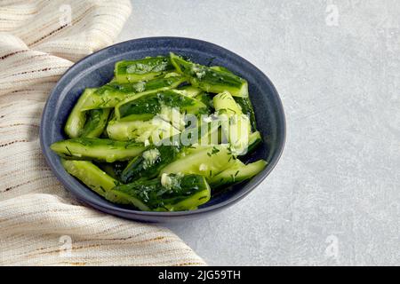 Smashed lightly salted broken cucumbers in a ceramic bowl surrounded by dill and kitchen towel napkin Stock Photo