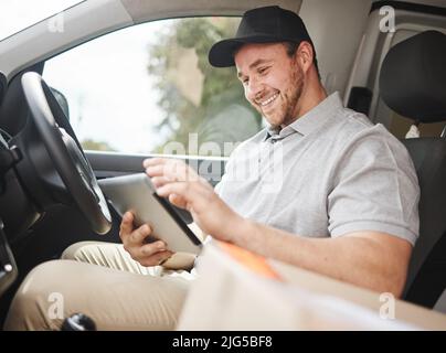 Looks like Im at the right place. Cropped shot of a handsome young delivery man using a tablet while sitting in his van. Stock Photo