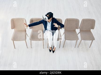 Immersed in a whole new world. High angle shot of a young businesswoman wearing a VR headset while sitting in line in an office. Stock Photo