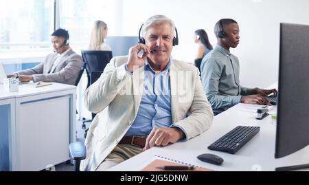 We call it mission possible. Portrait of a mature businessman using a headset and computer in a modern office. Stock Photo