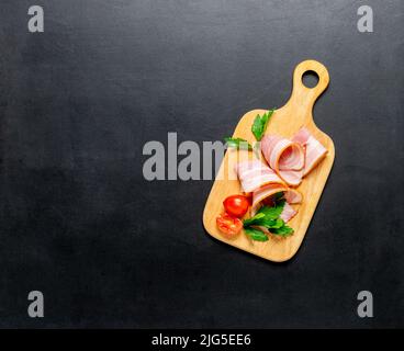 Meat food bacon slices ripe cherry tomatoes on a cutting wooden board on a black background, mocap Stock Photo