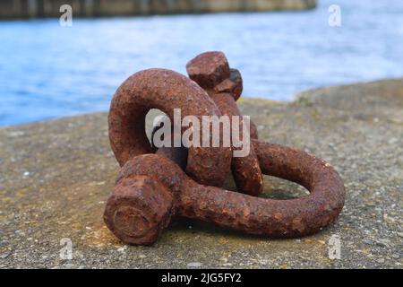 Rusty heavy metal shackle chain link resting on a concrete pier next to water Stock Photo