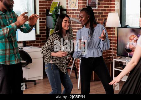 Multicultural people relaxing with music while enjoying wine party at home together. Diverse group of close friends dancing in living room while celebrating birthday event. Stock Photo