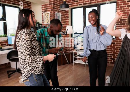 Joyful group of multiethnic people dancing and celebrating birthday at wine party event. Laughing friends in living room at home having fun together while listening to funky disco music. Stock Photo