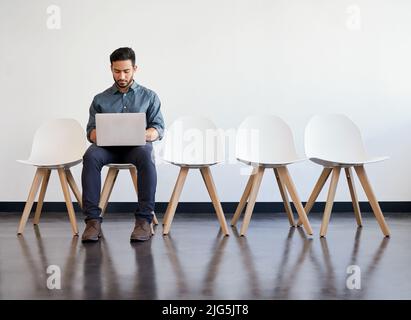Your time will come, stay ready. Shot of a young businessman using a laptop while waiting in line in a modern office. Stock Photo