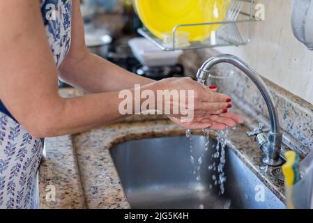 Young woman washing her hands at the kitchen sink. Stock Photo