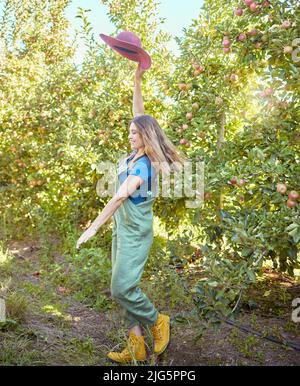 Cheerful farmer feeling optimistic and fulfilled for harvest season of fresh organic fruit. One excited energetic happy young woman jumping for joy on Stock Photo