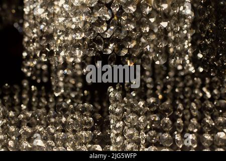 Texture of transparent glass in artificial light. Details of chandelier made of glass in dark. Chaotic background of glass in dim light. Stock Photo