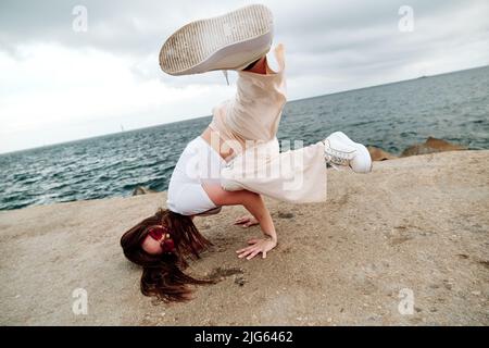 Female dancer doing handstand while breakdancing outdoors against sea. Stock Photo
