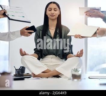 When you calm the inside, the outside will follow. Shot of a young businesswoman meditating on a desk in a demanding work environment. Stock Photo