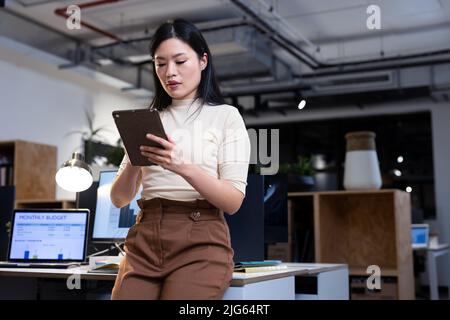 Low angle view of female asian professional working over digital pc while leaning on desk at night Stock Photo