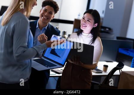 Happy multiracial colleagues analyzing charts over laptops while working late in office at night Stock Photo