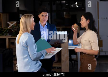 Multiracial businesswoman with report explaining data to coworkers while working late in office Stock Photo