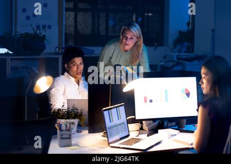 Multiracial professionals working and discussing over computers in modern office late at night Stock Photo