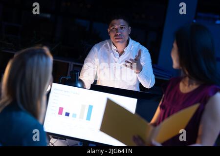 Multiracial businessman discussing with female workers while working late in modern office at night Stock Photo
