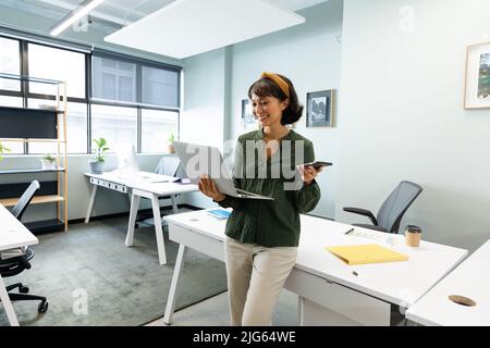 Asian female architect with smart phone using laptop in creative office Stock Photo