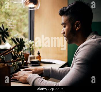 Young mixed race man or student browsing on a laptop in a cafe. One indian guy studying or working freelance at a restaurant. Typing to do research Stock Photo