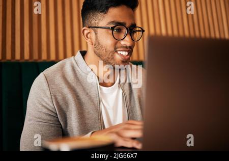 .. Handsome indian man with glasses sitting alone and using laptop in cafe. Man using wifi to browse the internet or doing freelance work in a cafe Stock Photo