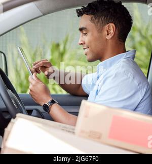 Monitoring it all on his digital system. Shot of a young delivery man using a digital tablet while sitting in a van. Stock Photo