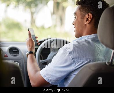 He never gets lost while going about logistics. Shot of a young delivery man using a cellphone while sitting in a van. Stock Photo