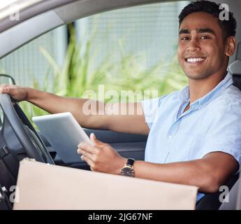 Ill be pulling up with your package next. Portrait of a young delivery man using a digital tablet while sitting in a van. Stock Photo