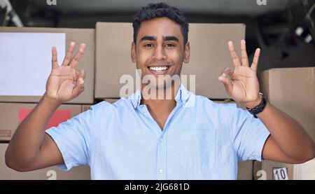 Your parcel is in safe hands with me, I promise. Portrait of a young delivery man gesturing an okay sign while loading boxes from a van. Stock Photo